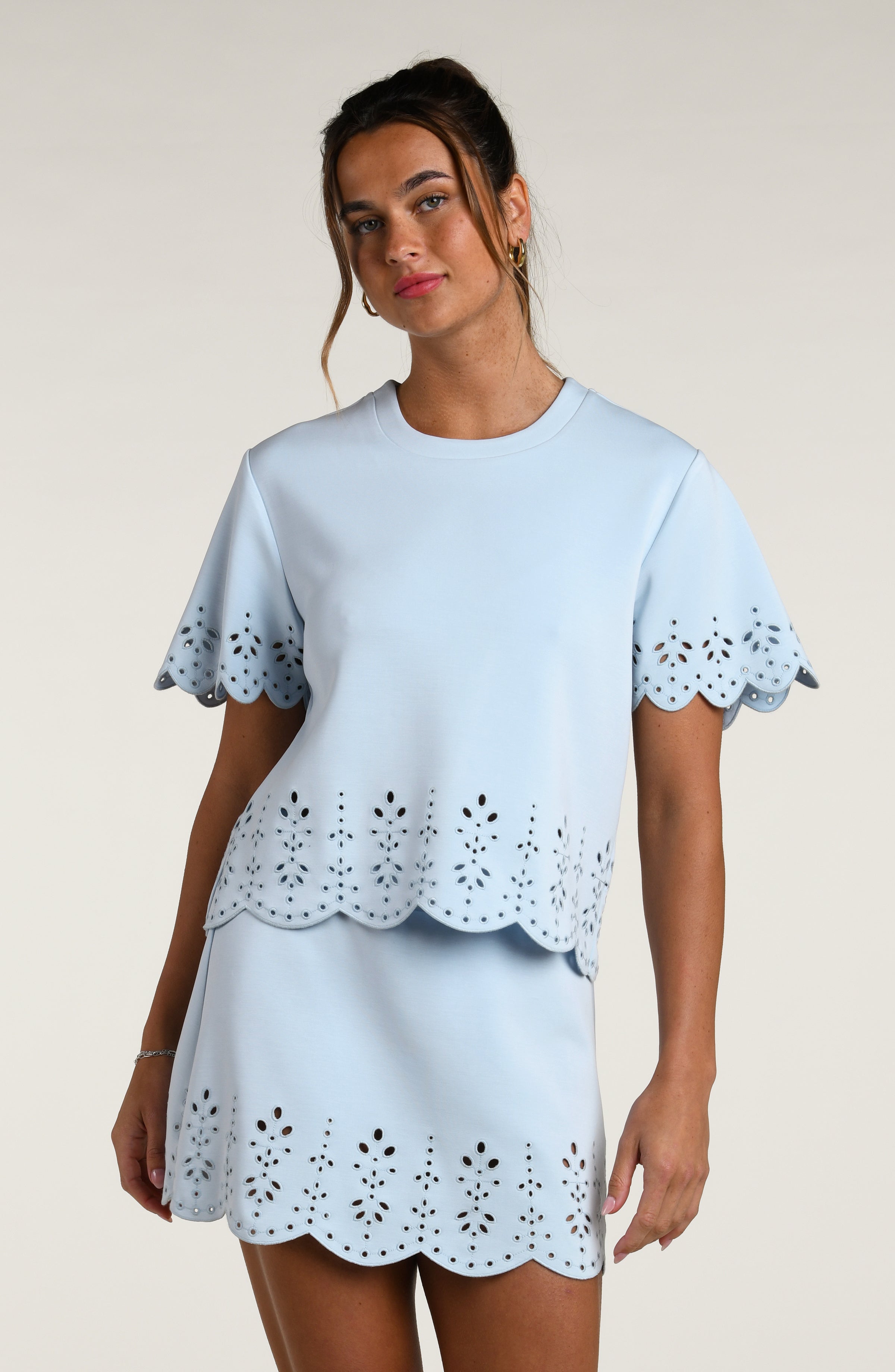 Woman wearing a light blue short sleeve top with scalloped edges and a matching skirt on a plain background