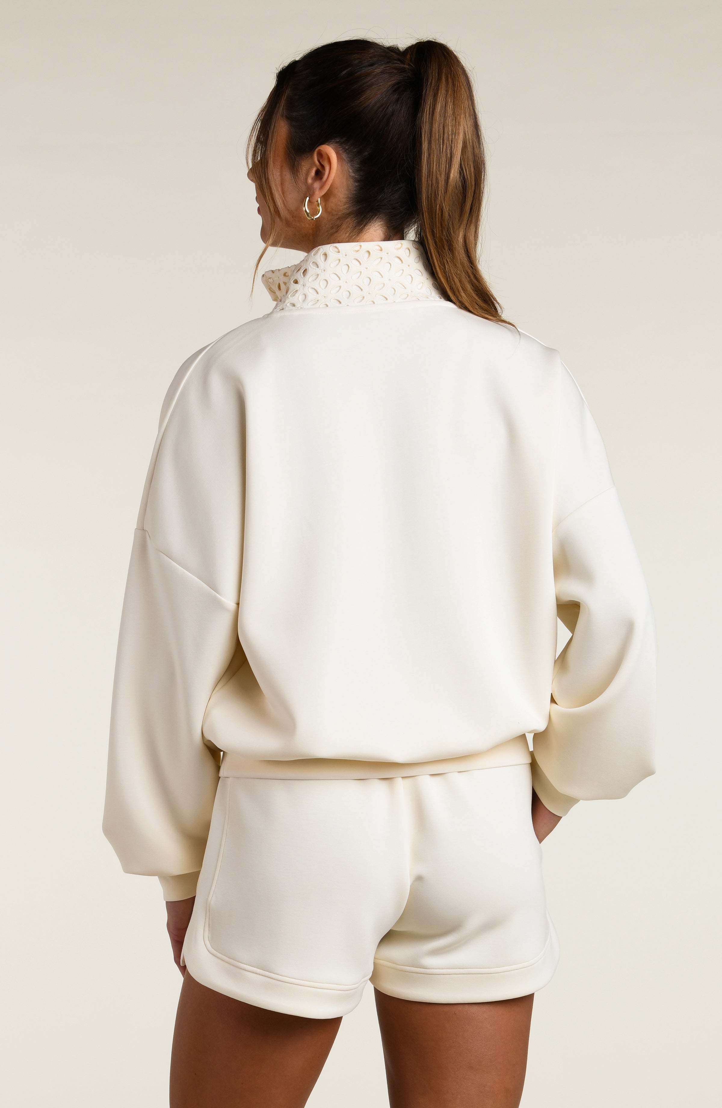 Woman wearing a beige pullover with lace detailing and matching shorts on a beige background