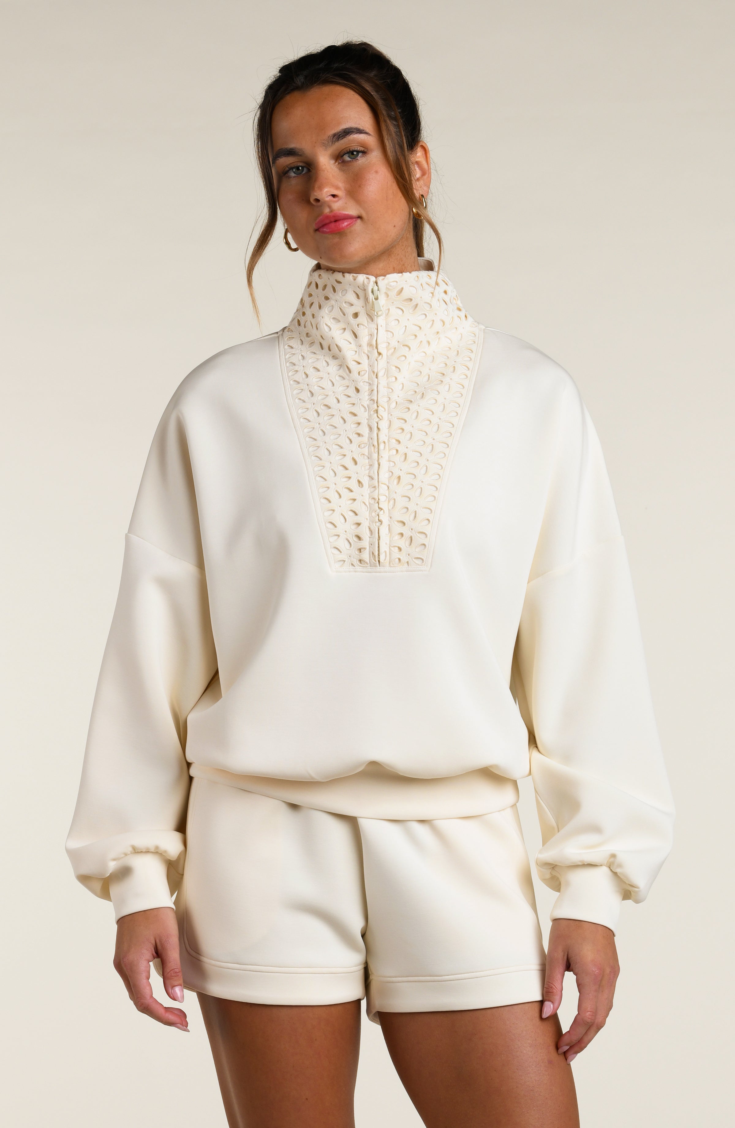 Woman wearing a beige pullover with lace detailing and matching shorts on a beige background