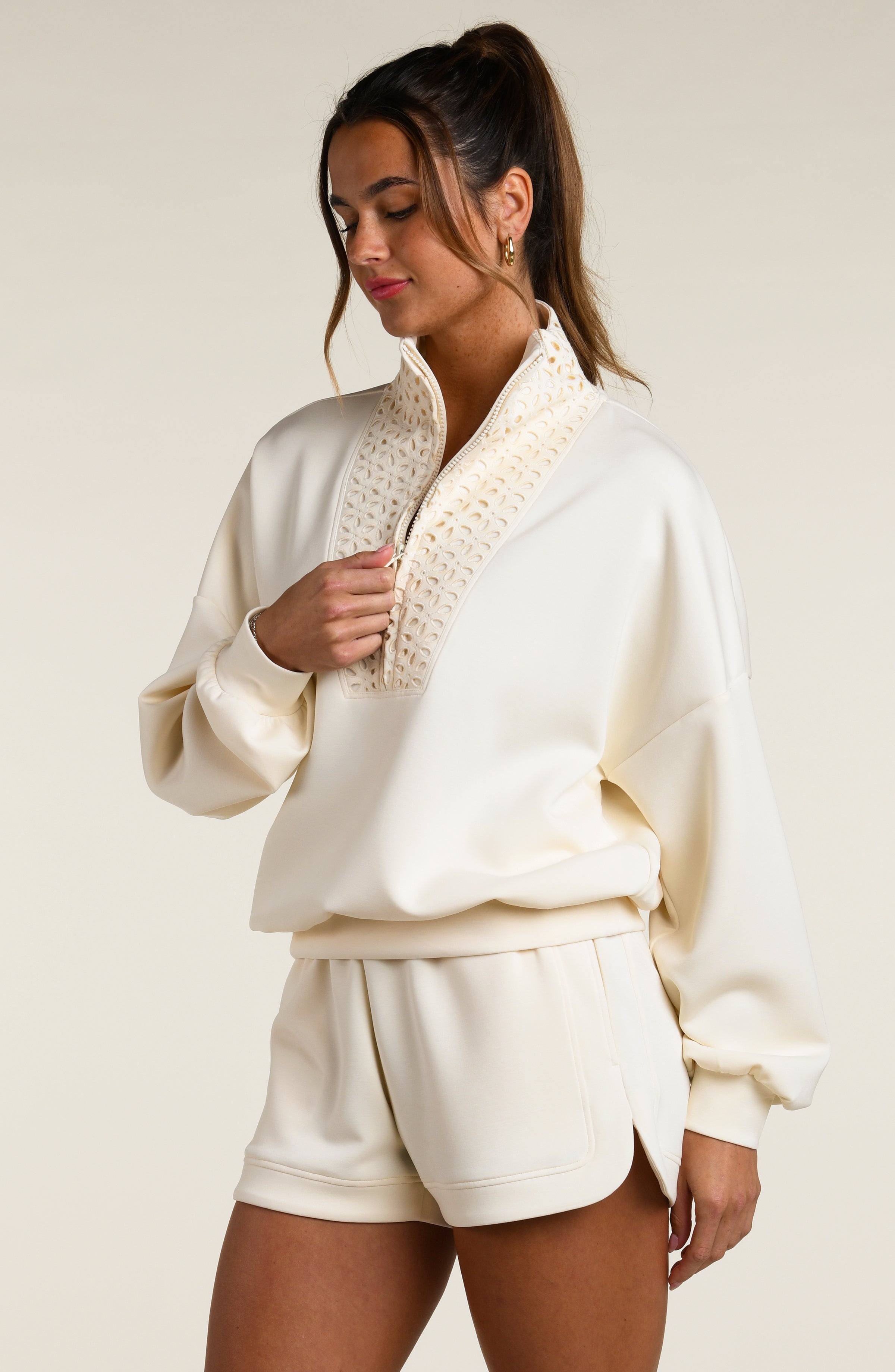 Woman wearing a cream-colored sweatshirt with a high-neck top and shorts on a plain background