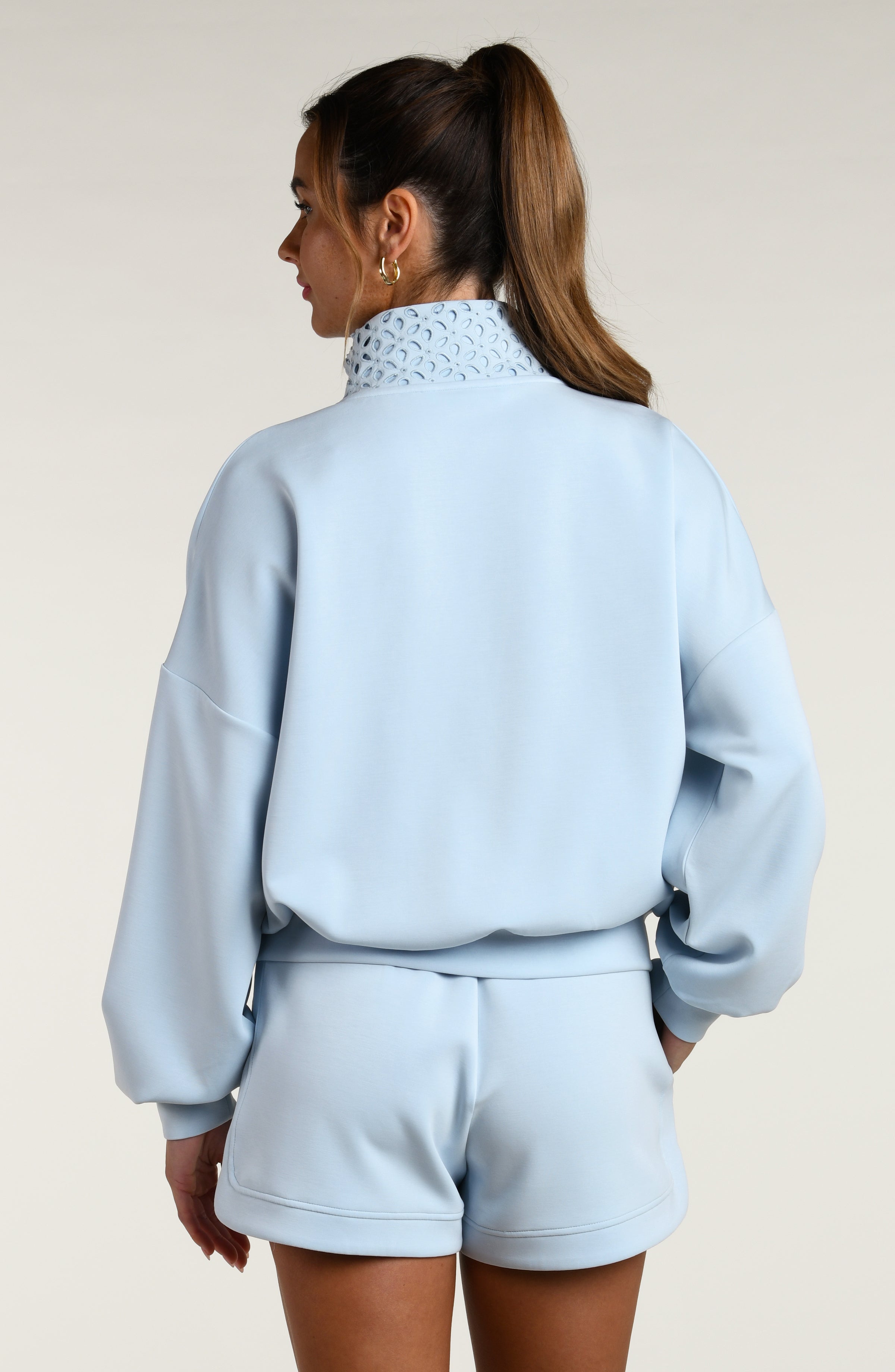 Woman wearing a light blue tracksuit with a lace collar on a beige background