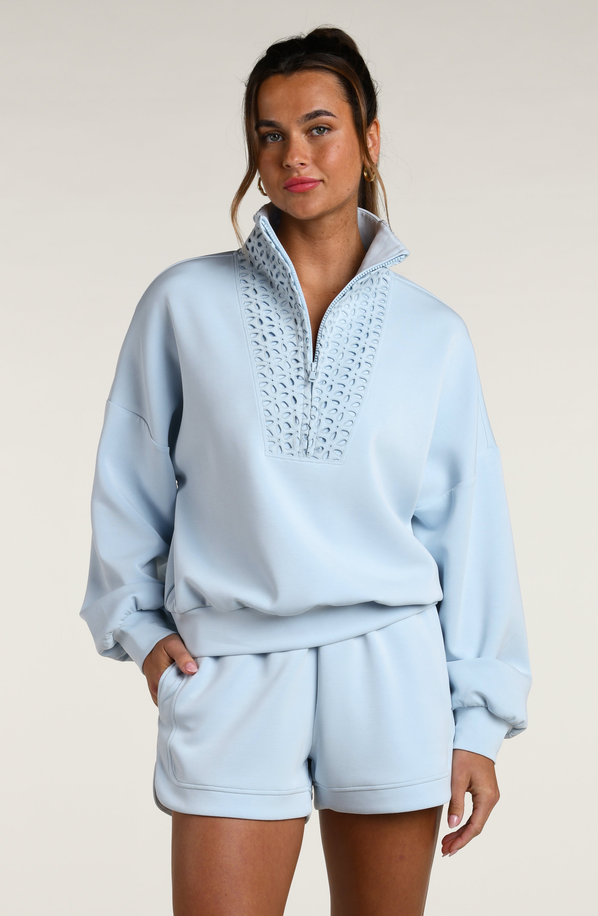 Woman wearing a light blue pullover with lace detailing and matching shorts on a beige background