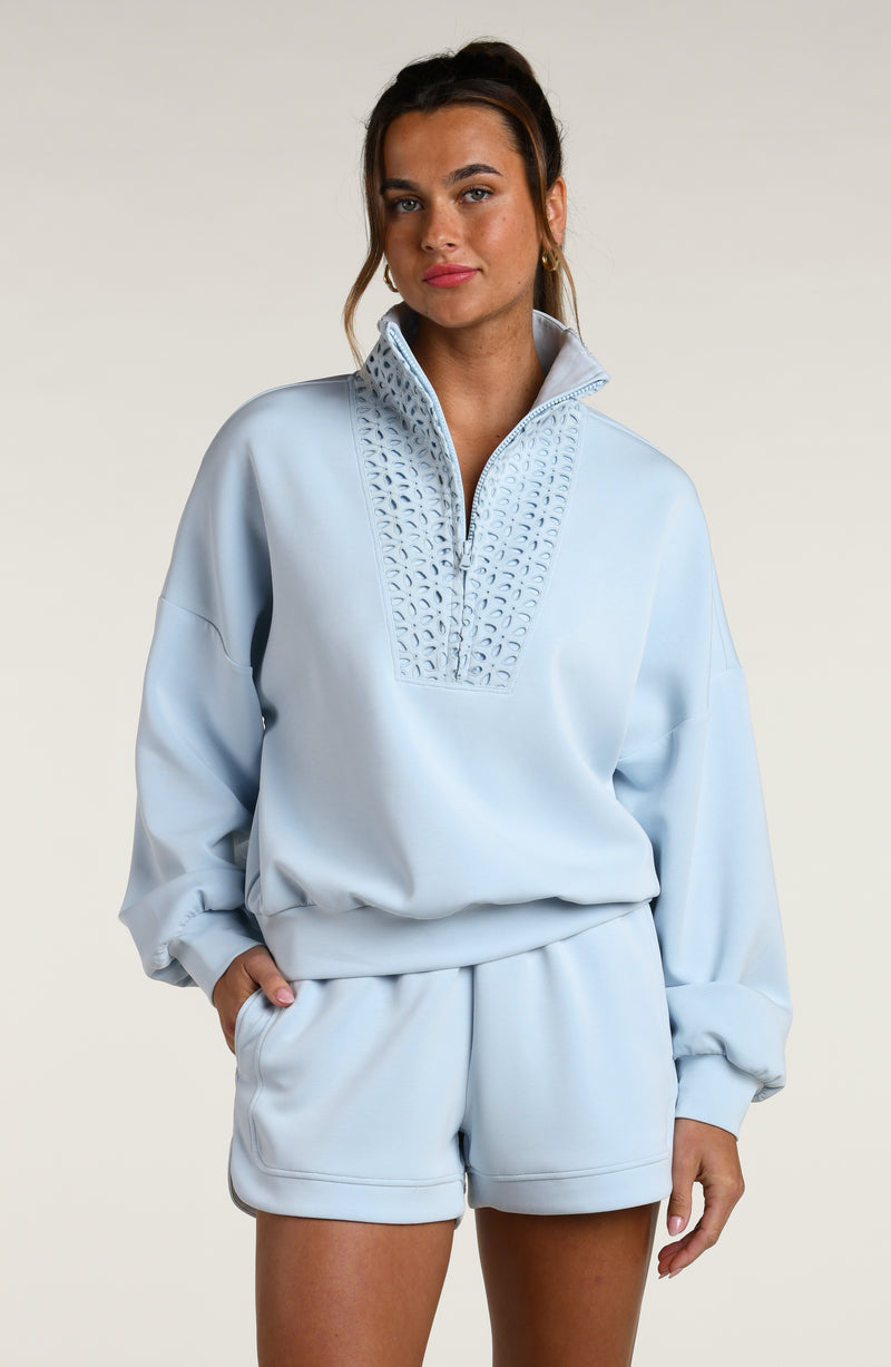 Woman wearing a light blue pullover with lace detailing and matching shorts on a beige background