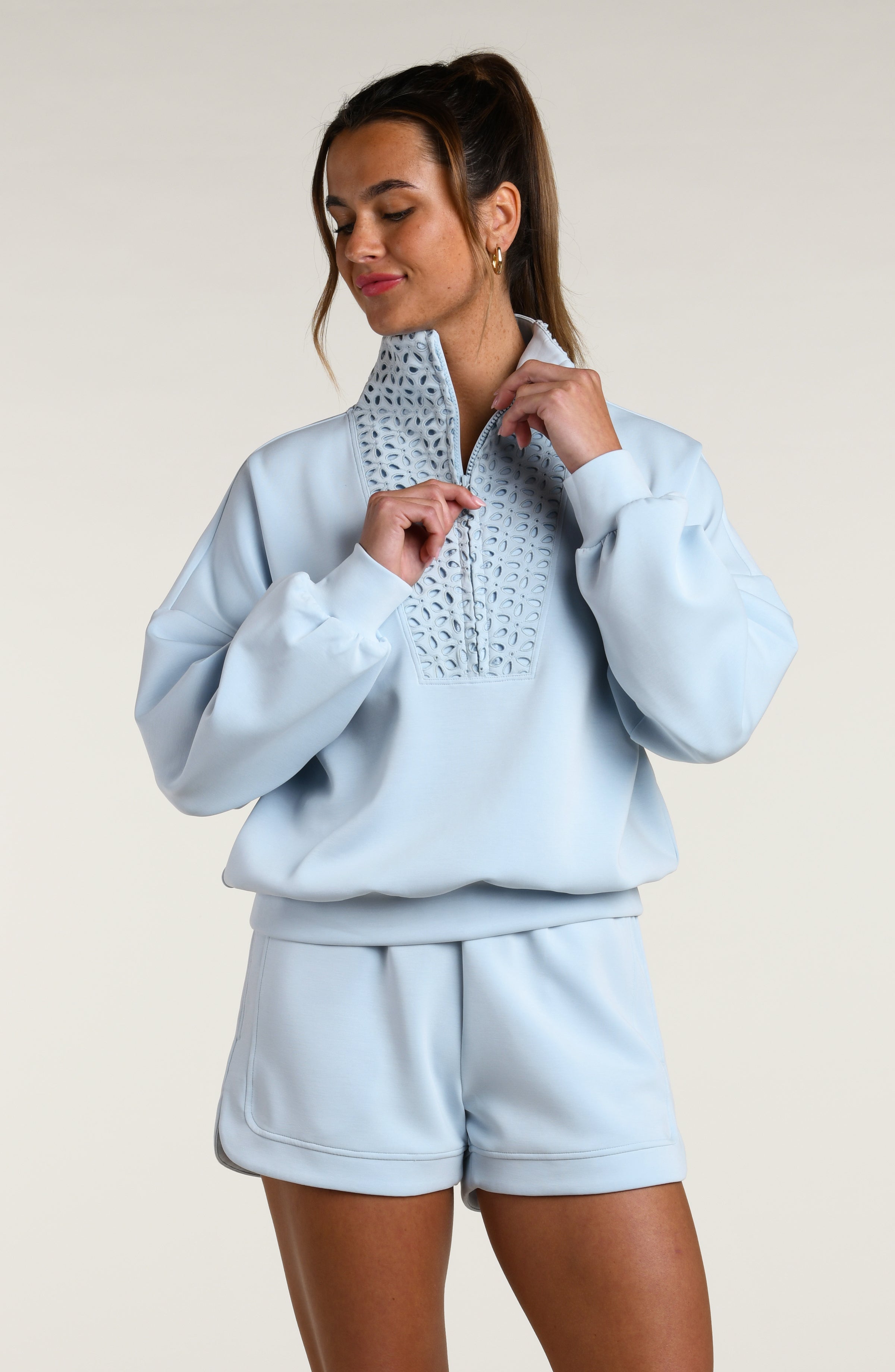 Woman wearing a light blue sweatshirt with lace detailing and matching shorts on a plain background