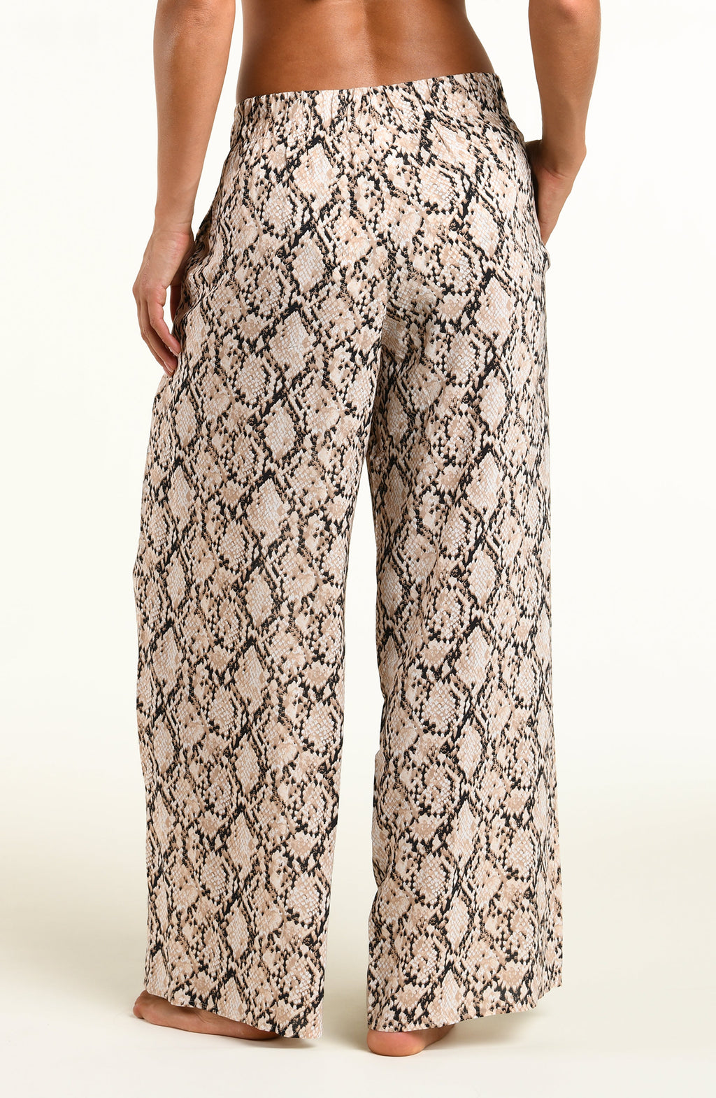 Wide-leg pants with a beige and black snakeskin pattern, shown on a model from the back against a plain light background.