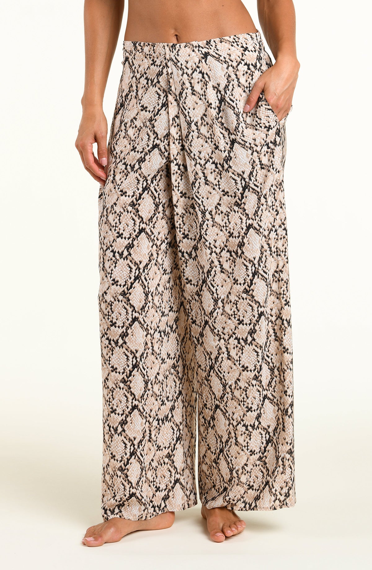 A person wearing loose, wide-leg pants with a beige, black, and brown snakeskin pattern, shown from the waist down against a plain light background.