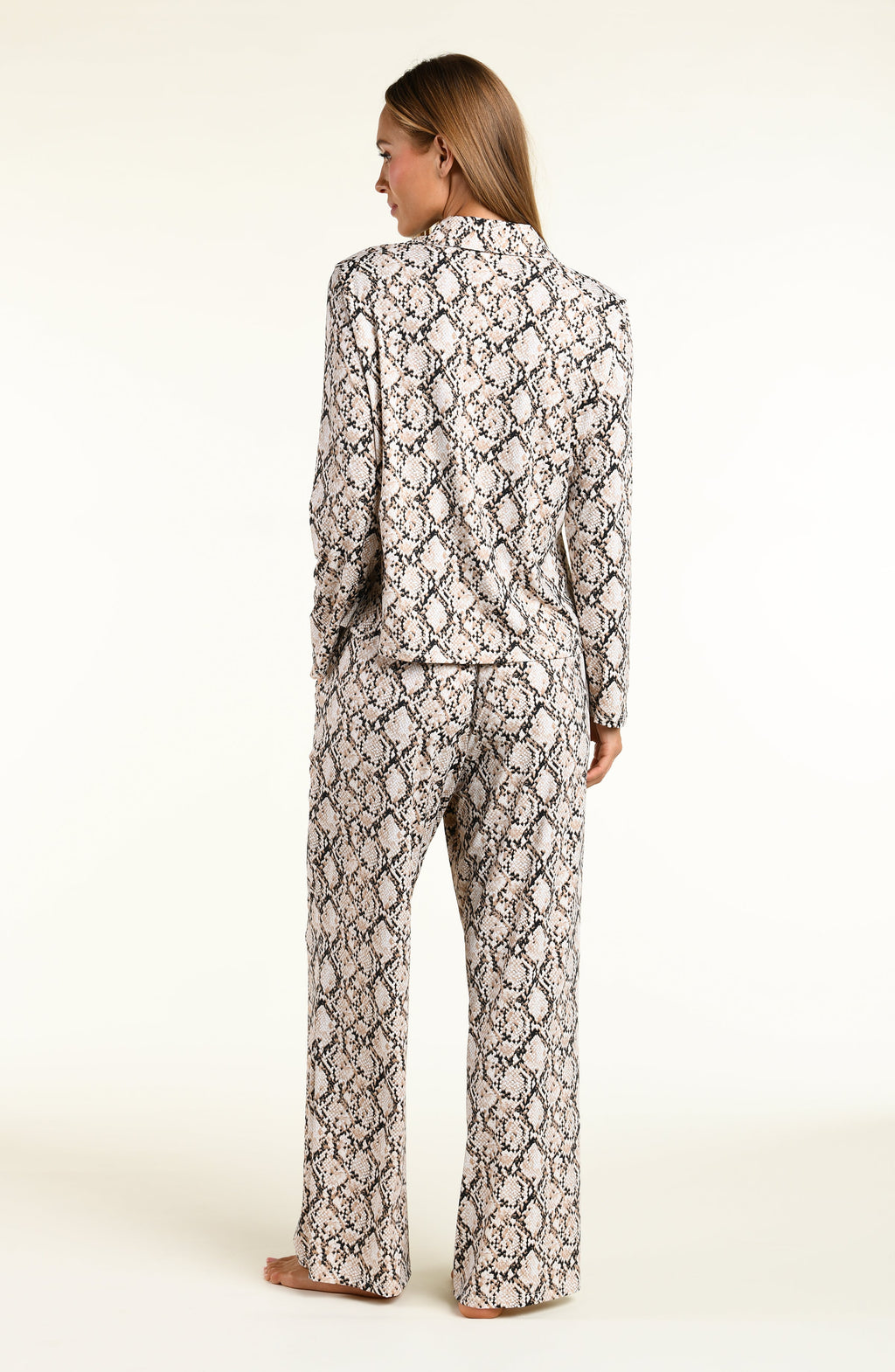 A woman shown from the back wearing a matching long-sleeve top and wide-leg pants set in a beige, black, and white snakeskin pattern, set against a plain off-white studio background.