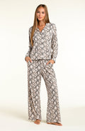 A woman modeling a matching two-piece pajama set with a beige, black, and white snakeskin pattern, standing against a plain off-white studio background.
