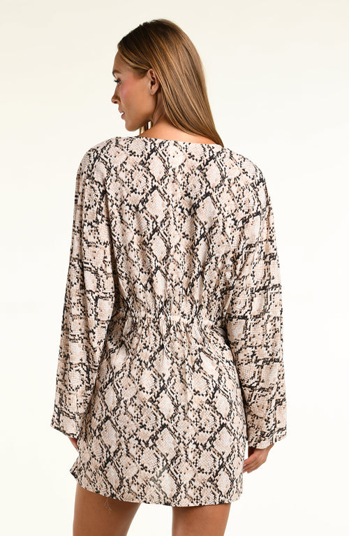 A woman modeling a long-sleeve tunic with a beige, black, and brown snakeskin pattern against a plain light background.