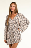 A woman modeling a long-sleeve tunic with a beige, black, and brown snakeskin pattern against a plain light background.