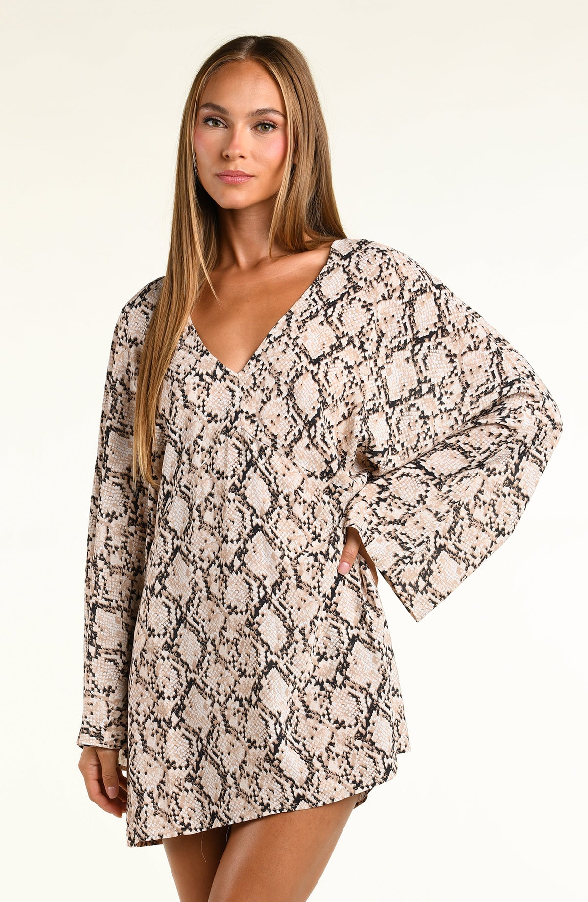 A woman modeling a long-sleeve tunic with a beige, black, and brown snakeskin pattern against a plain light background.