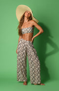 A woman modeling a two-piece snakeskin print set consisting of a bandeau bikini top and matching wide-leg pants, photographed against a green studio background.