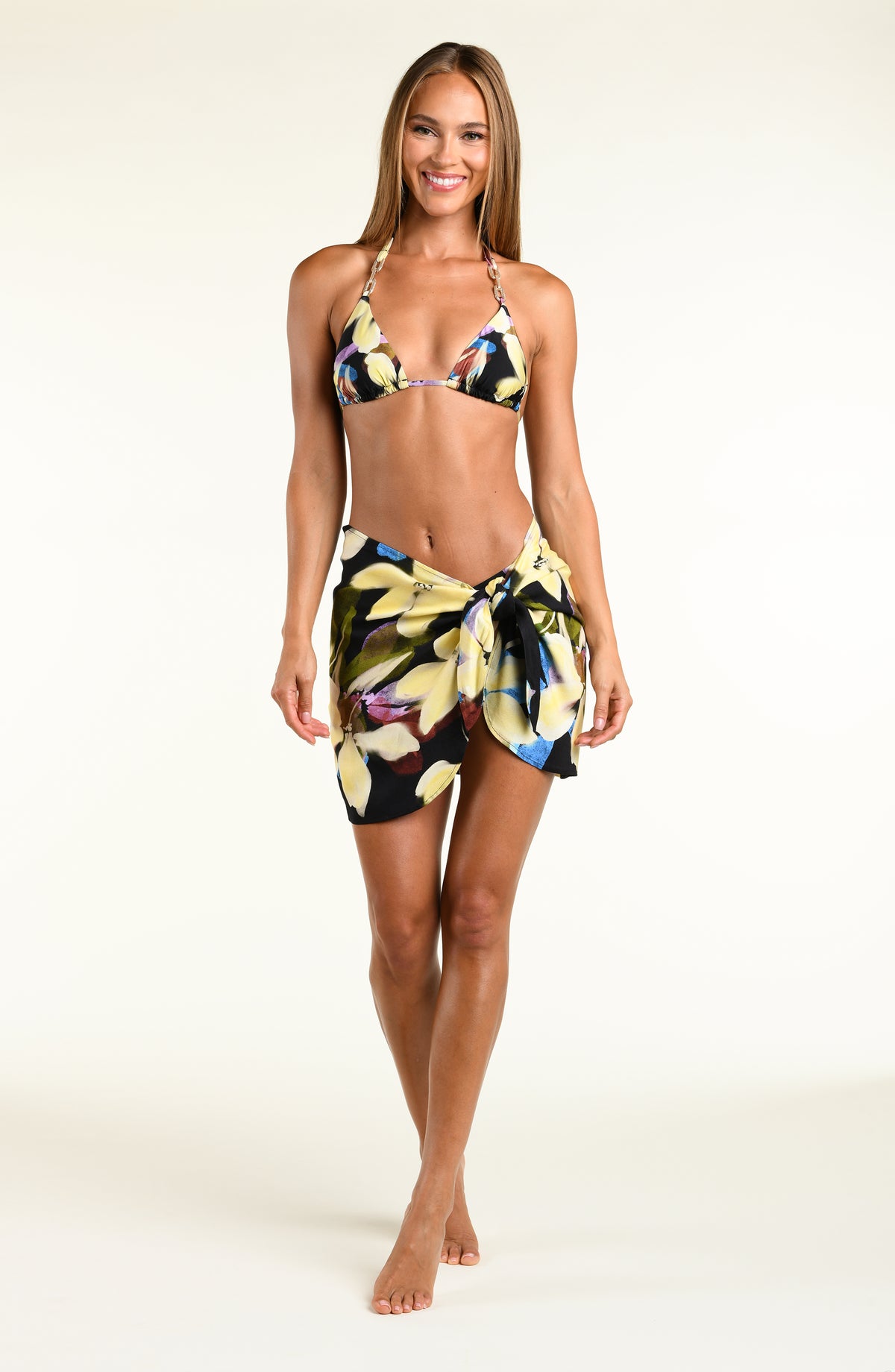 A model wearing a vibrant yellow, blue, and green floral printed bikini top and matching wrap sarong against a white background. 
