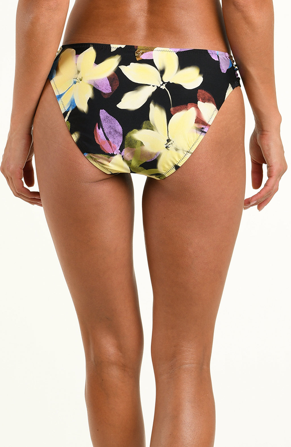 A model wearing a pair of bikini bottoms with a black background and a yellow, purple, and white floral print, shown against a plain white studio background.