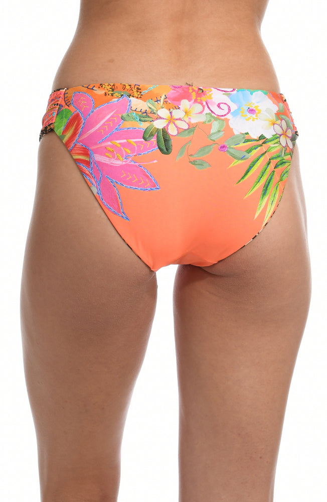 Model is wearing an orange multicolored tropical printed side shirred hipster bikini bottom from our In A Trance collection. 