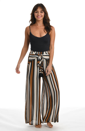 
            
                Load image into Gallery viewer, Model is wearing a retro inspired printed beach pant swimsuit cover up with diagonal stripes and floral medallions in brown earthy tones from our 70&amp;#39;s Stripe collection.
            
        