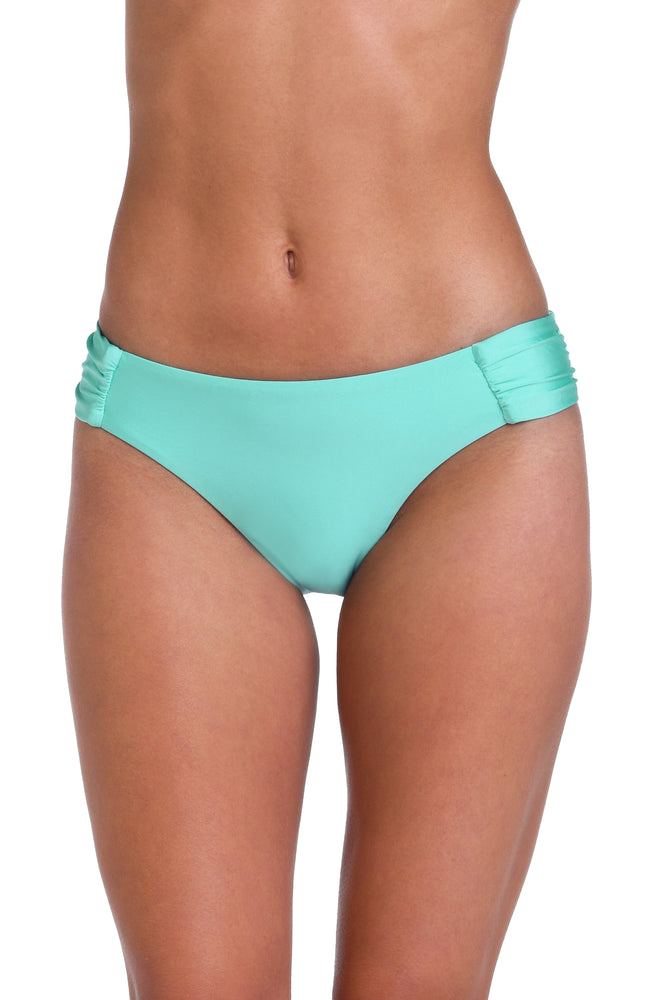 Model is wearing a solid pale, greenish-blue (seaglass) colored side shirred hipster swimsuit bottom.