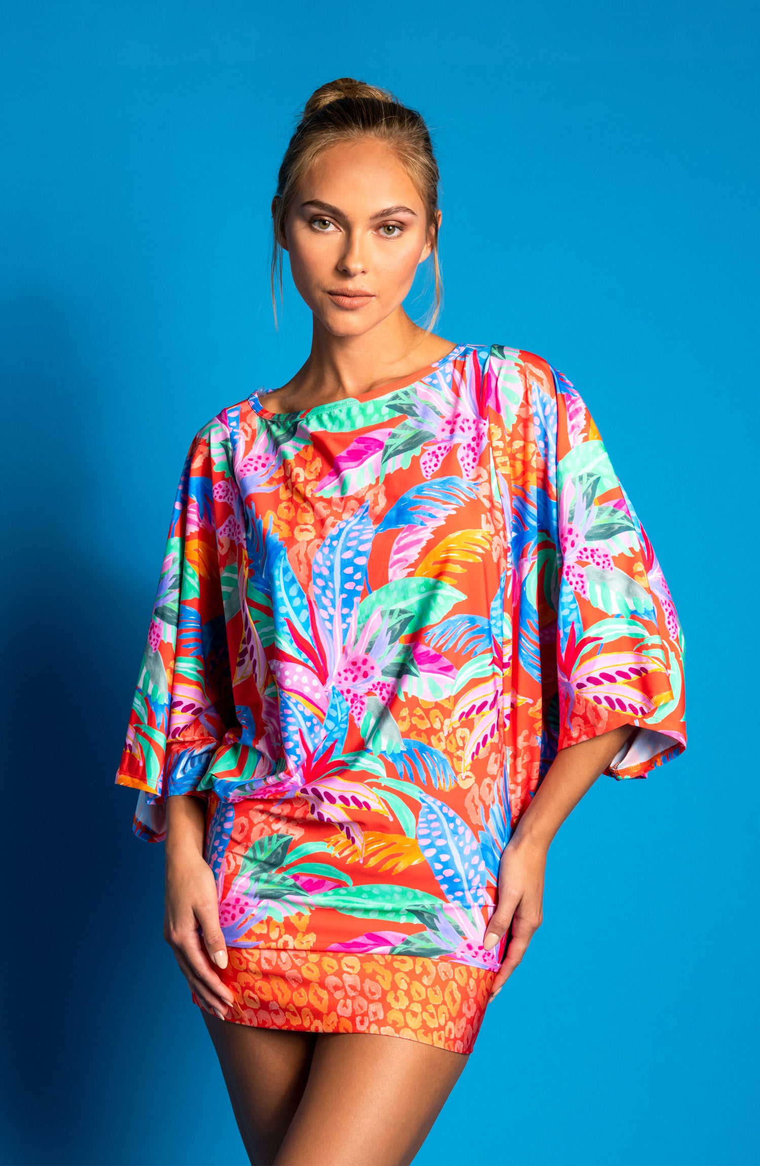 Model wearing a tropical print tunic swimwear cover-up on a blue background.