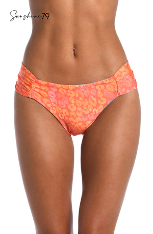 
            
                Load image into Gallery viewer, Model is wearing an orange multicolored tropical printed reversible side shirred hipster bikini bottom from our Sunshine 79 brand.
            
        