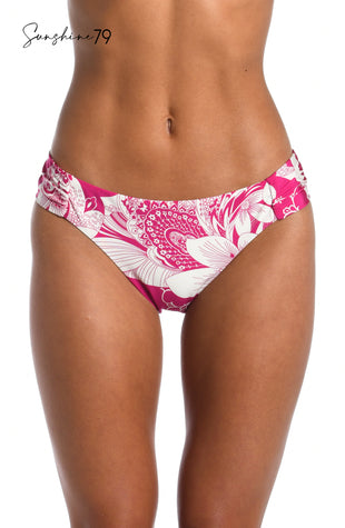 Model is wearing a fuchsia and white multicolored tropical printed side shirred hipster bikini bottom from our Sunshine 79 brand.