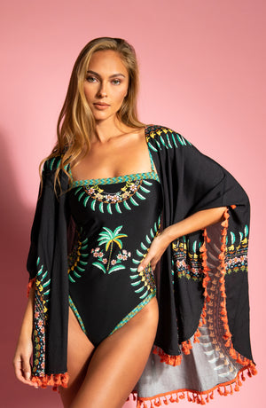 Model wearing a tropical print bandeau one piece with a matching cover-up on a pink background.