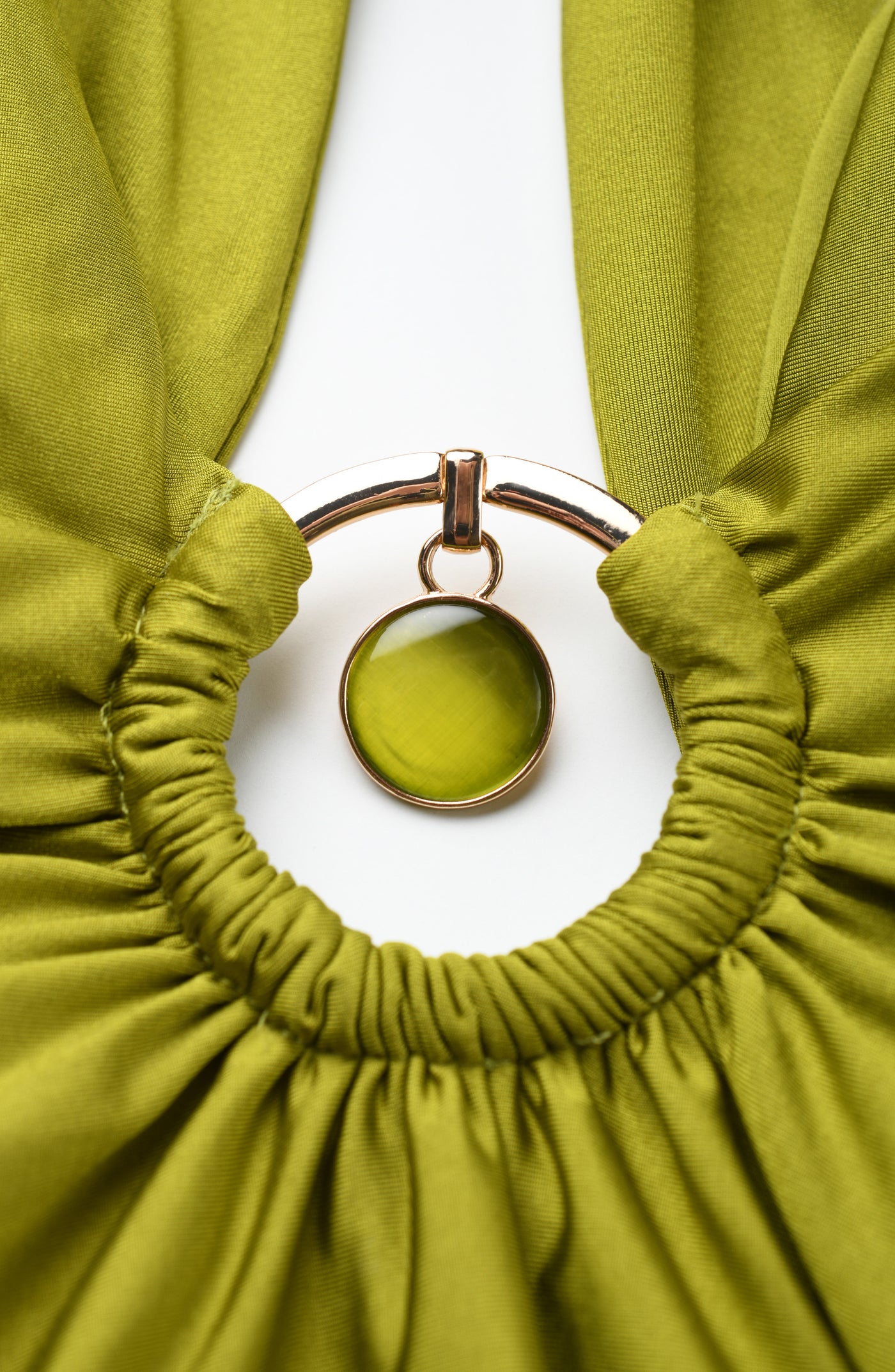 
                  
                    Olive green fabric with a gold ring and pendant on a white background
                  
                