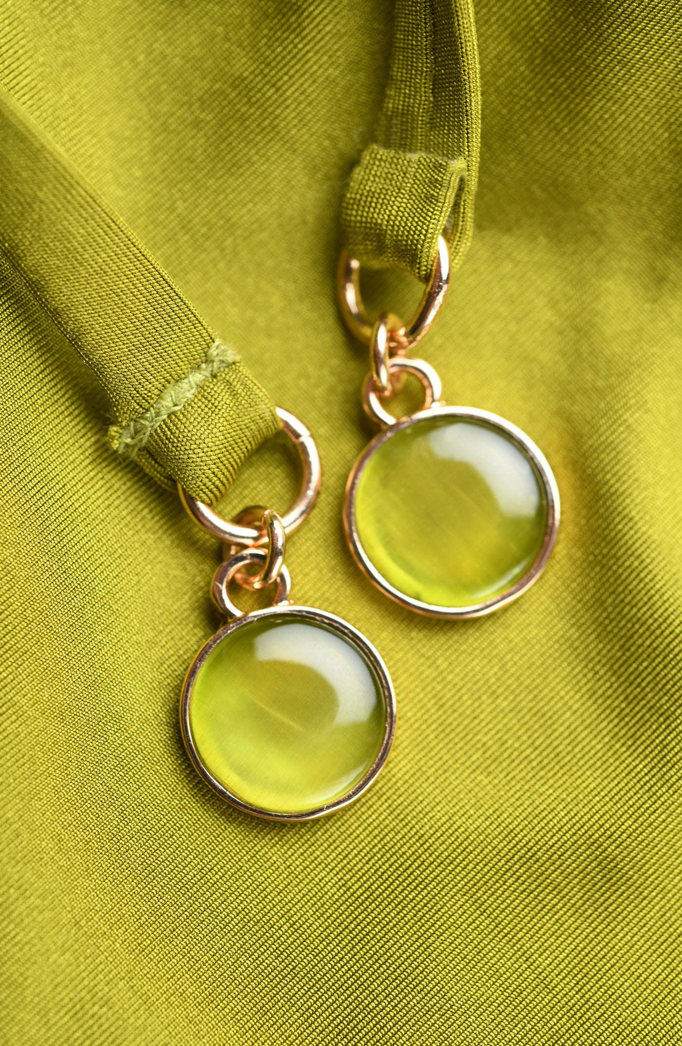 
                  
                    Close-up of olive green gold charms on tassels against a green background.
                  
                