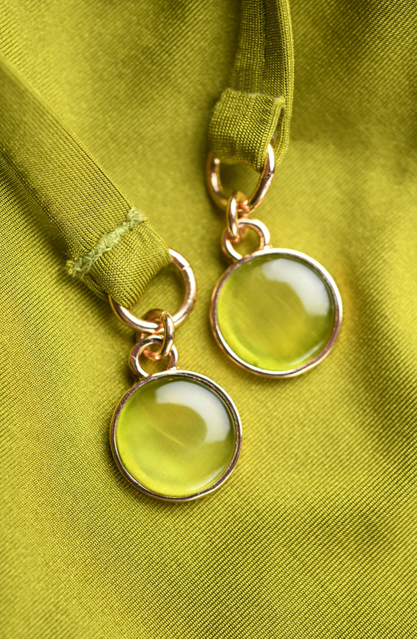 Close-up of olive green gold charms on tassels against a green background.