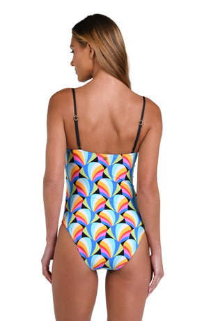 Model is wearing a pink, blue, yellow, and orange multicolored over the shoulder triangle bikini top on a geometric patterned black background.