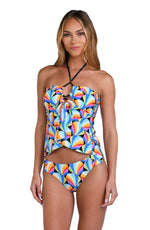 Model is wearing a pink, blue, yellow, and orange multicolored bandeau tankini top on a geometric patterned black background.