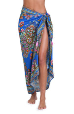 Model is wearing a pink, orange, teal, and green multicolored floral patterned pareo swimsuit cover up set against an indigo blue background.