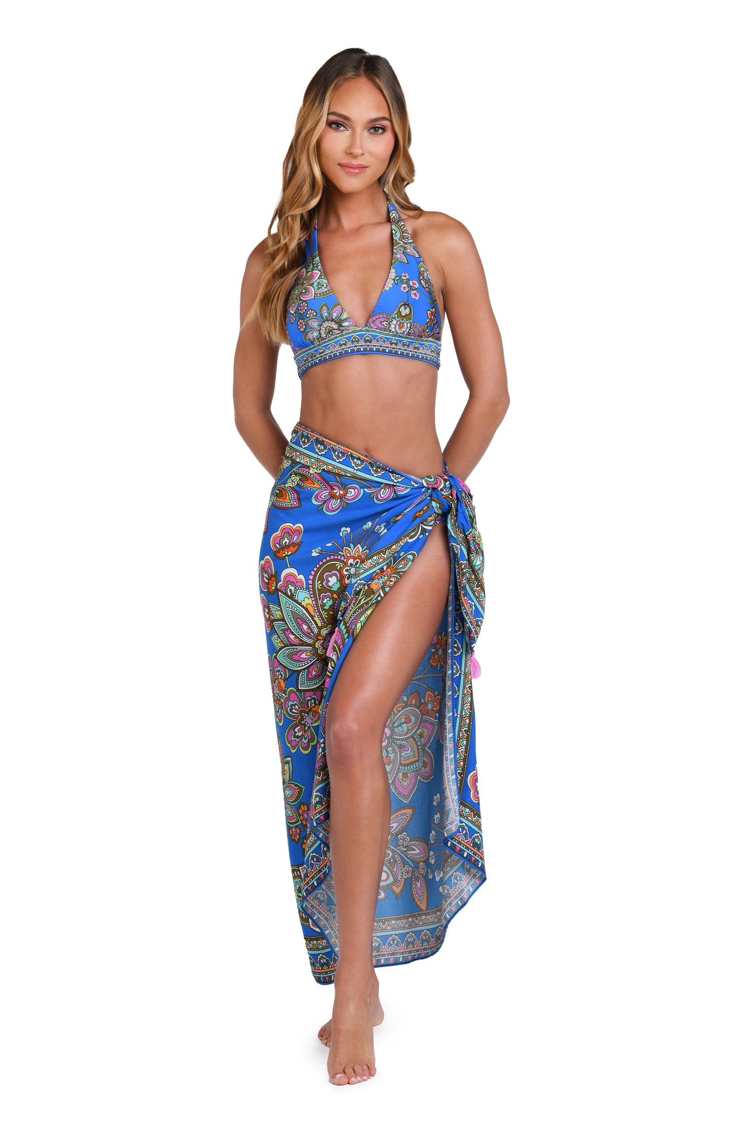 Model is wearing a pink, orange, teal, and green multicolored floral patterned pareo swimsuit cover up set against an indigo blue background.