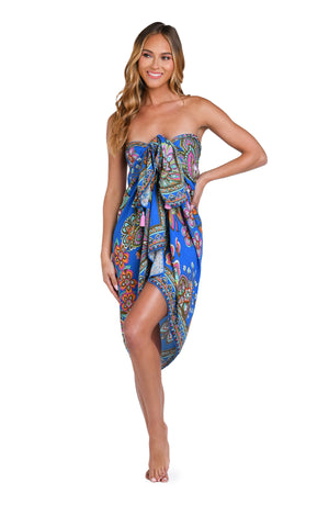 Model is wearing a pink, orange, teal, and green multicolored floral patterned pareo swimsuit cover up set against an indigo blue background.