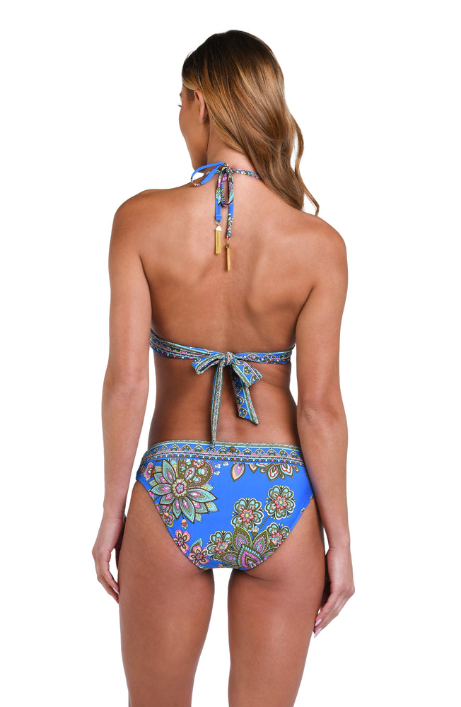 Model is wearing a pink, orange, teal, and green multicolored floral patterned banded halter bikini top set against an indigo blue background.