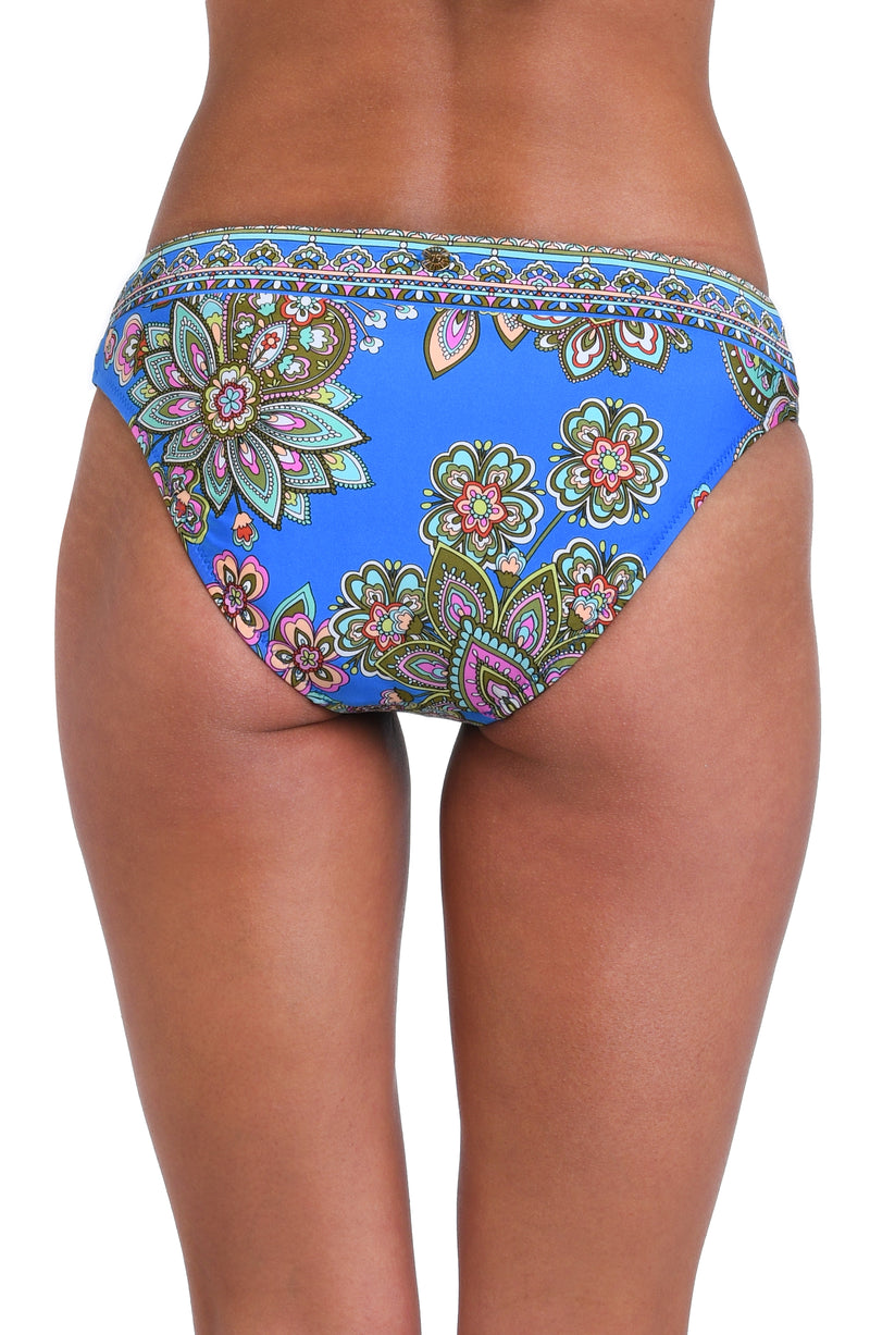 Model is wearing a pink, orange, teal, and green multicolored floral patterned hipster swimsuit bottom set against an indigo blue background.