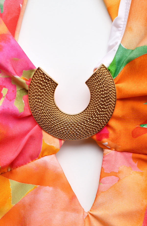 Close-up of a gold front charm on a multicolored tropical printed one piece swimsuit. 