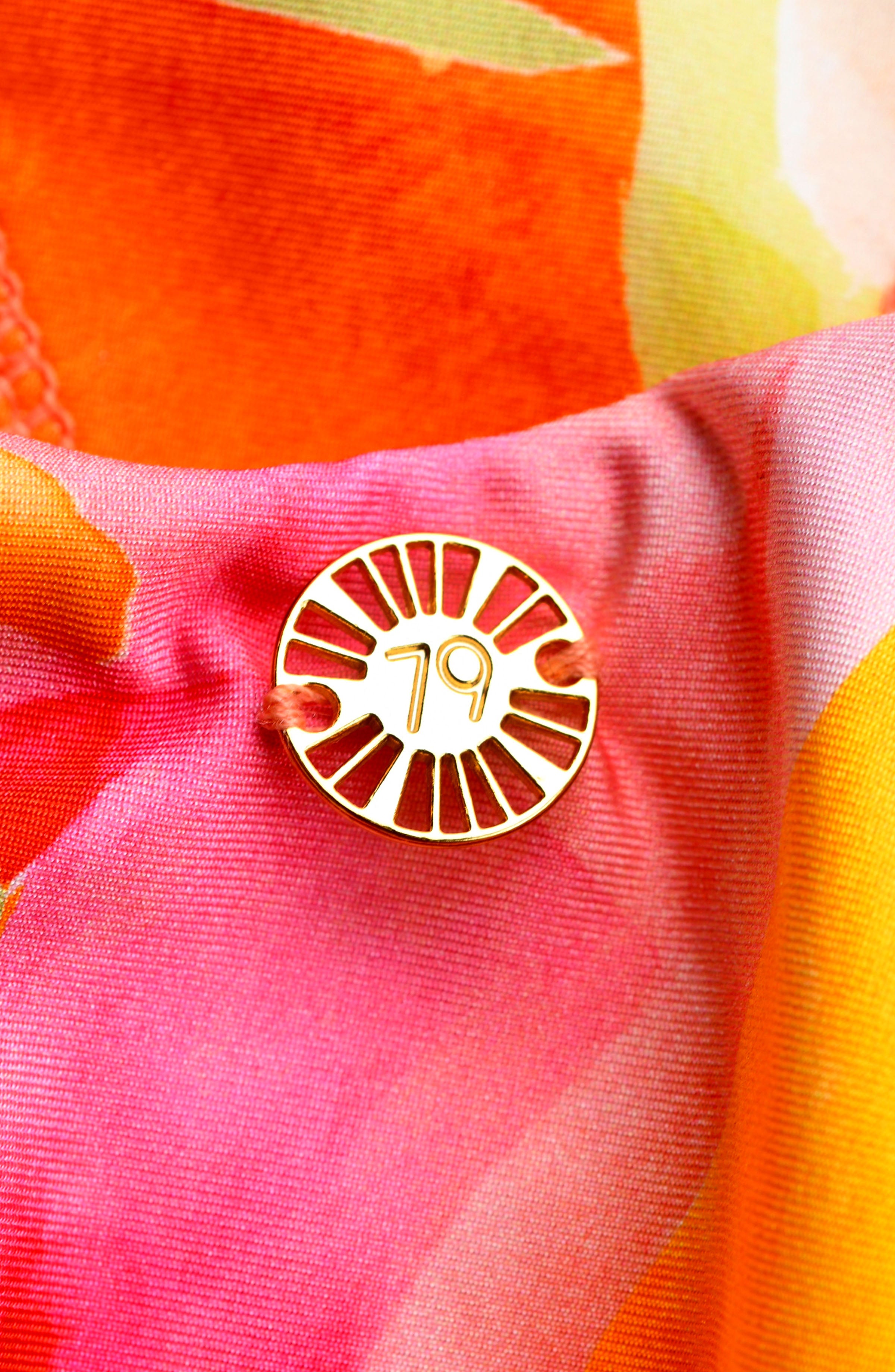 Close-up of a gold front charm on a multicolored tropical printed one piece swimsuit. 