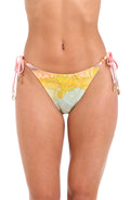Front image of model wearing a multi-colored pastel yellow, green, and peach patterned hipster bikini swimsuit bottom featuring side ties and tassels.