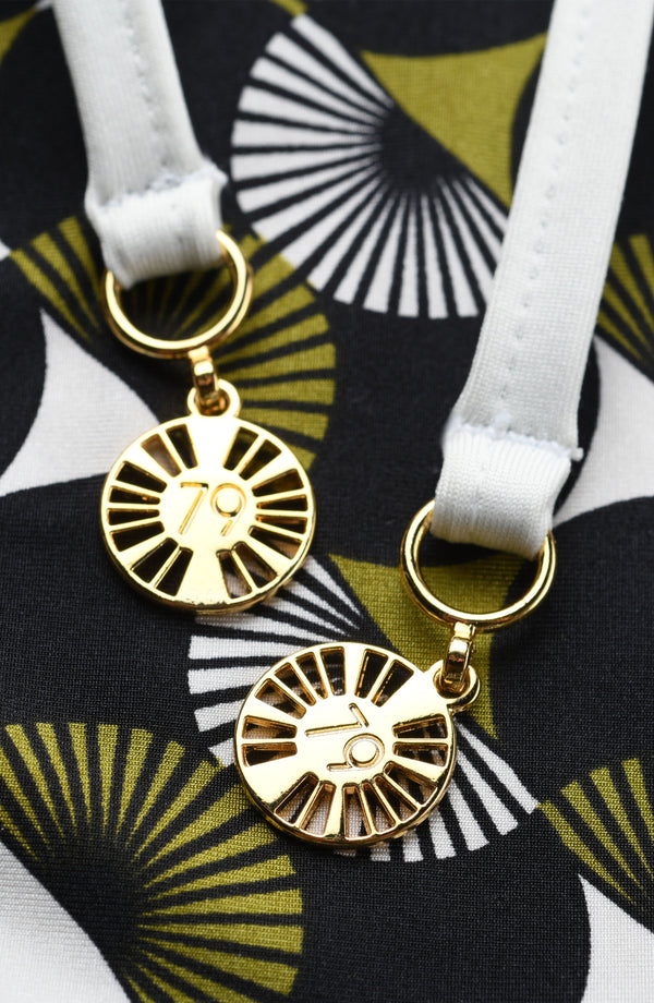 Gold charm on a white strap against a patterned background