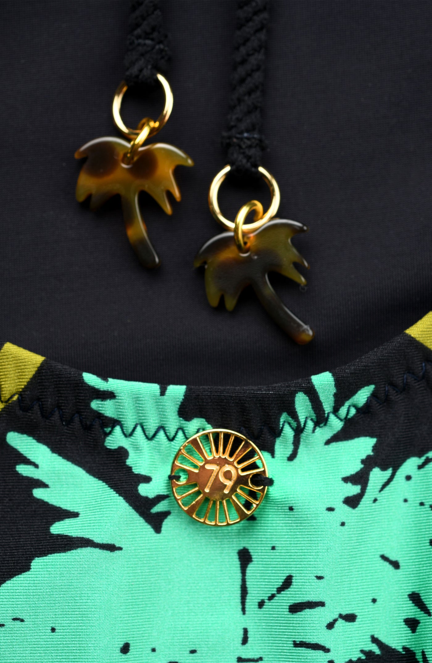 
                  
                    Gold palm tree charms on a black and green fabric background
                  
                