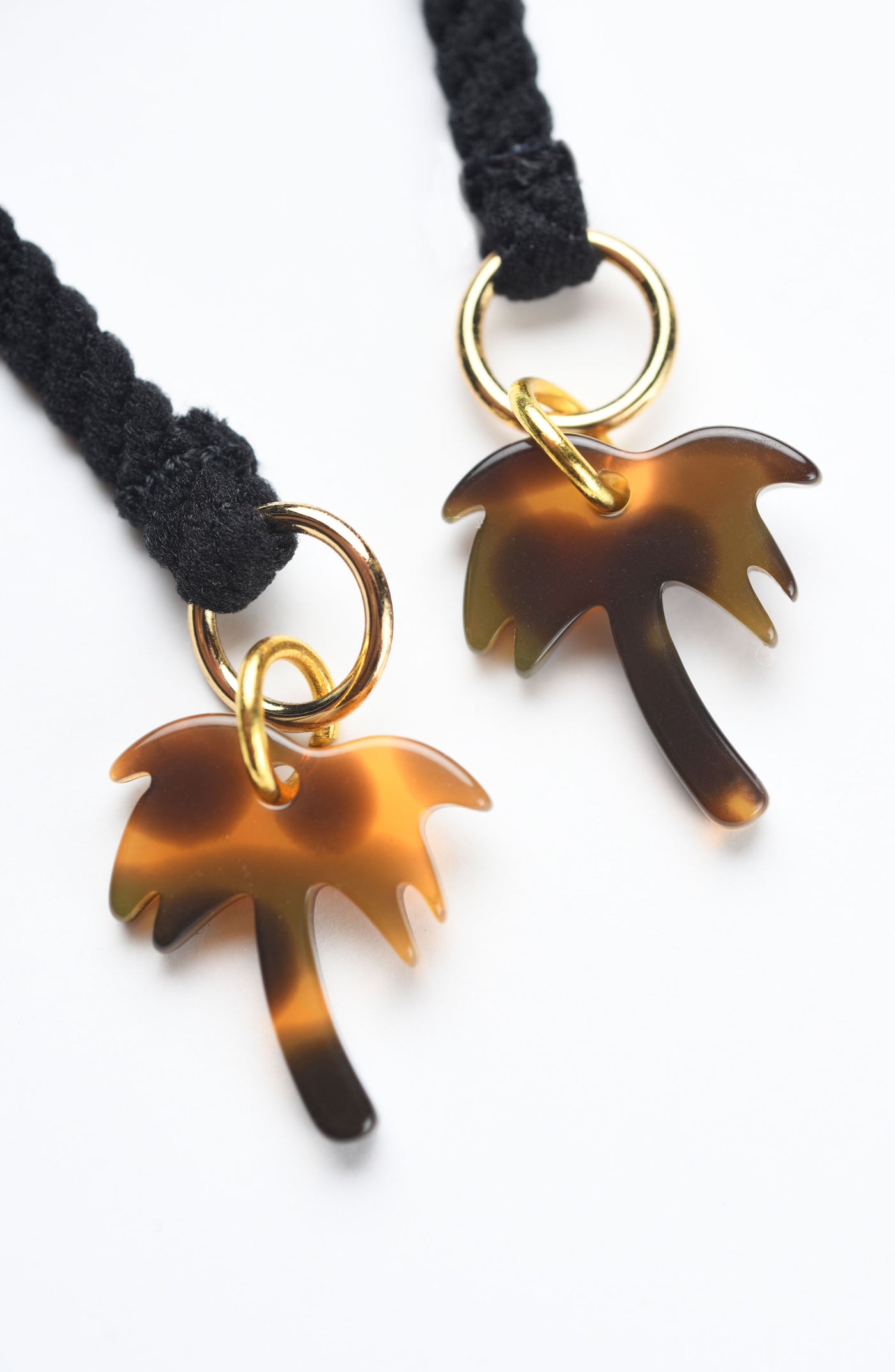 
                  
                    Close-up of gold palm tree tassel charms against a white background. 
                  
                