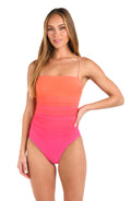 Front image of model wearing a one piece bandeau swimsuit with thin spaghetti straps, featuring an Ombre design in vibrant orange and pink. 