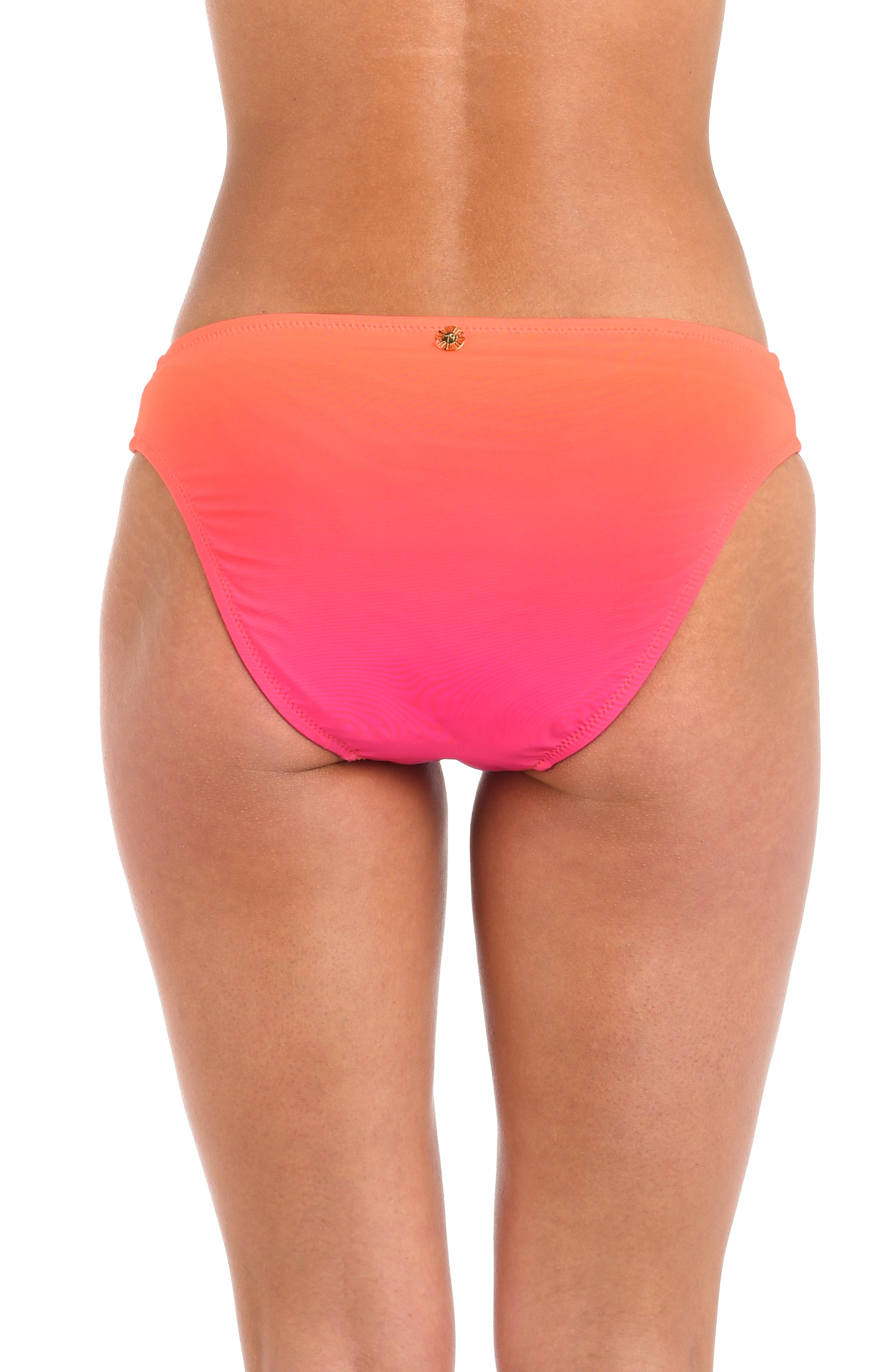 Back image of model wearing a hipster bikini swimsuit bottom with side shirring, gold charm, and moderate rear coverage, featuring an Ombre design in vibrant orange and pink. 