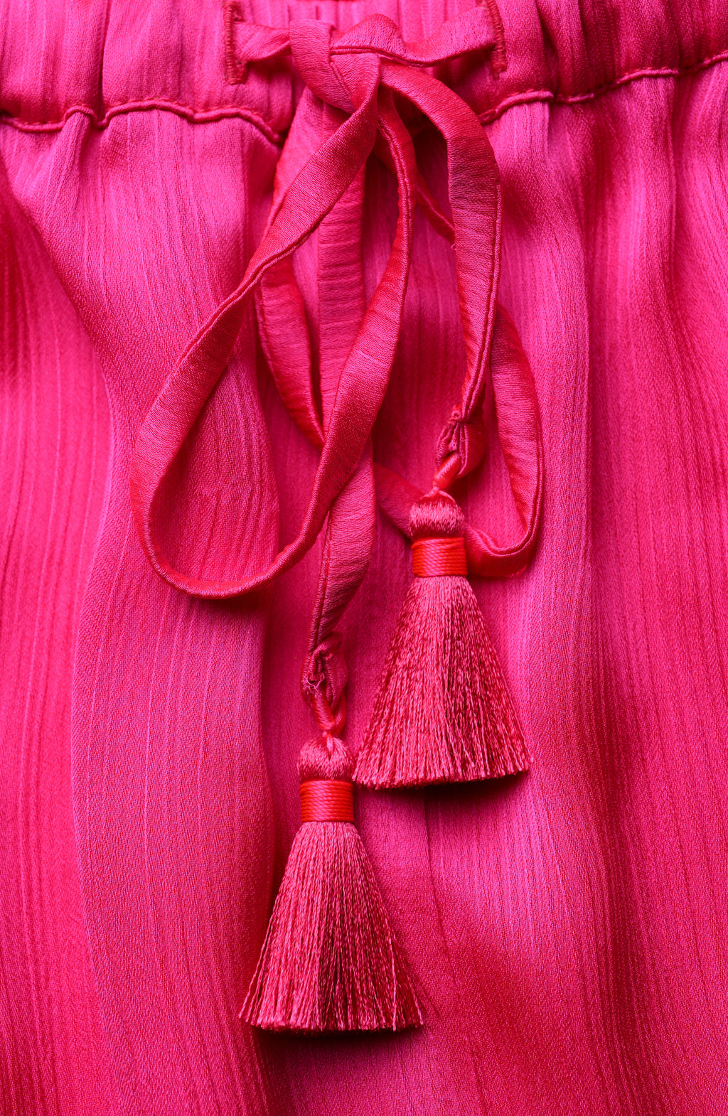 Close-up of a pink fabric with tassels on a matching pink background