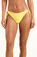 A model wearing a bright yellow string bikini bottom with side-tie details, shown from the waist to the upper thighs against a plain white studio background.