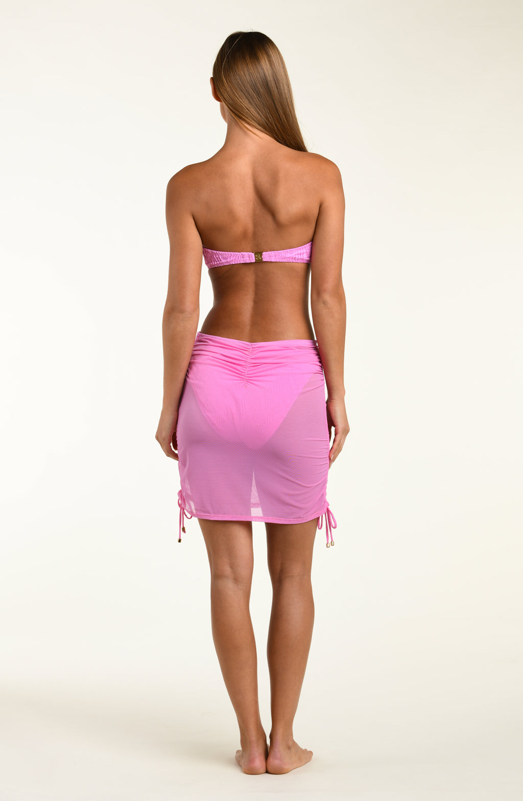 Woman wearing a pink bikini top and matching mesh cover up skirt against a white background.