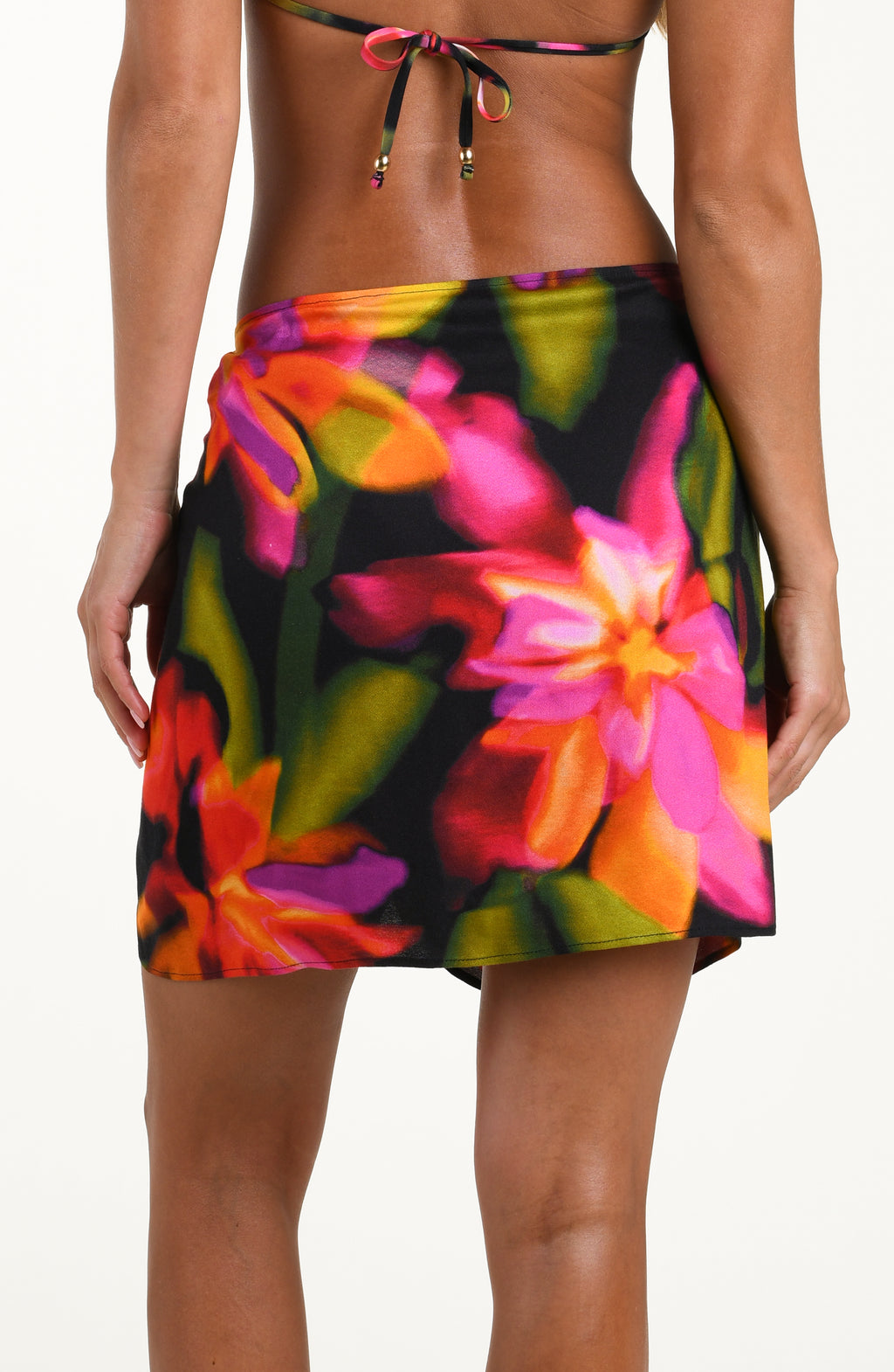 Back image of model wearing a short pareo cover up with a gold slider, featuring a bright floral print.