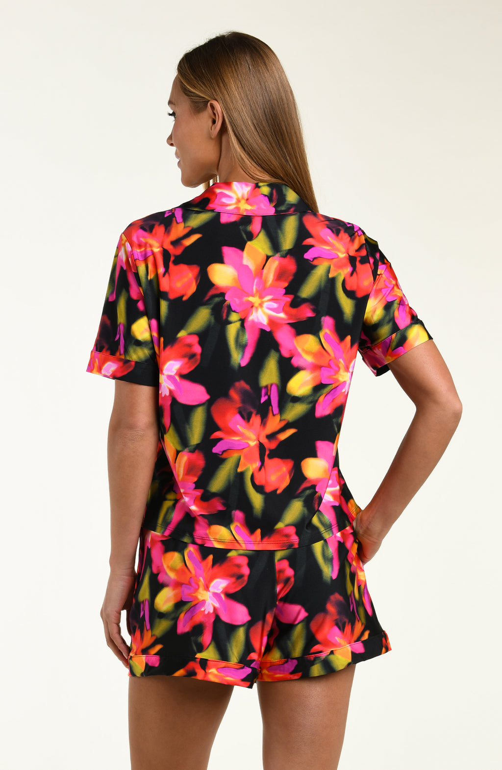 Woman wearing a colorful floral shirt and short pajama set on a white background