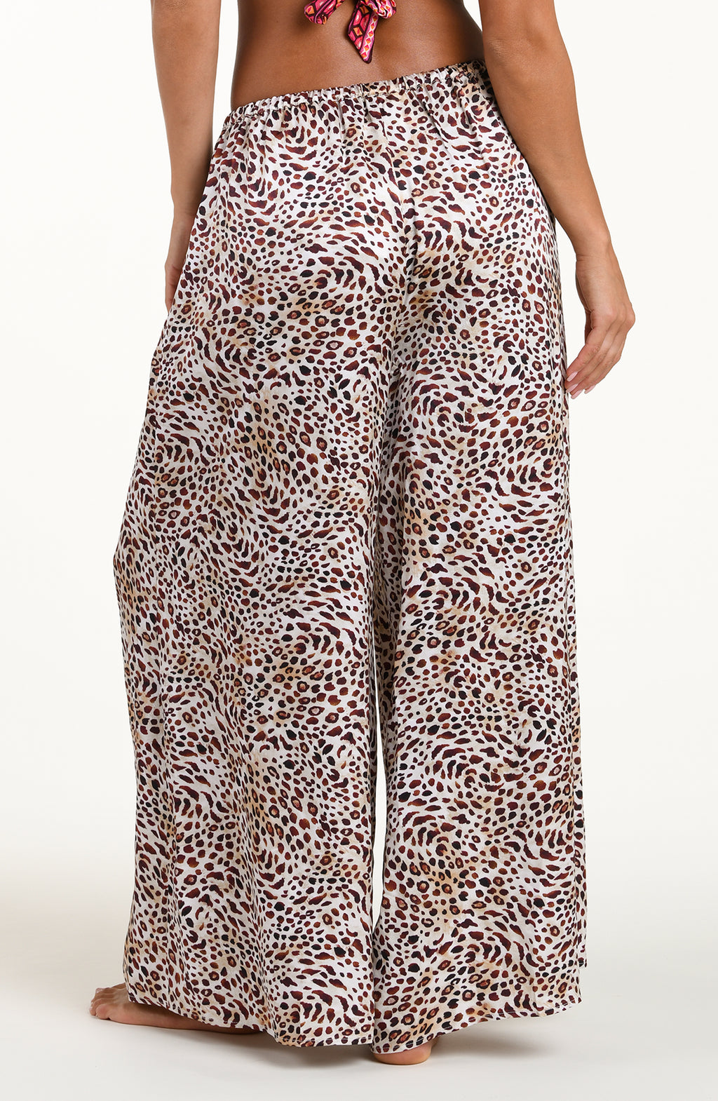 Back image of model wearing leopard printed beach pants with an elastic waist and pockets. 