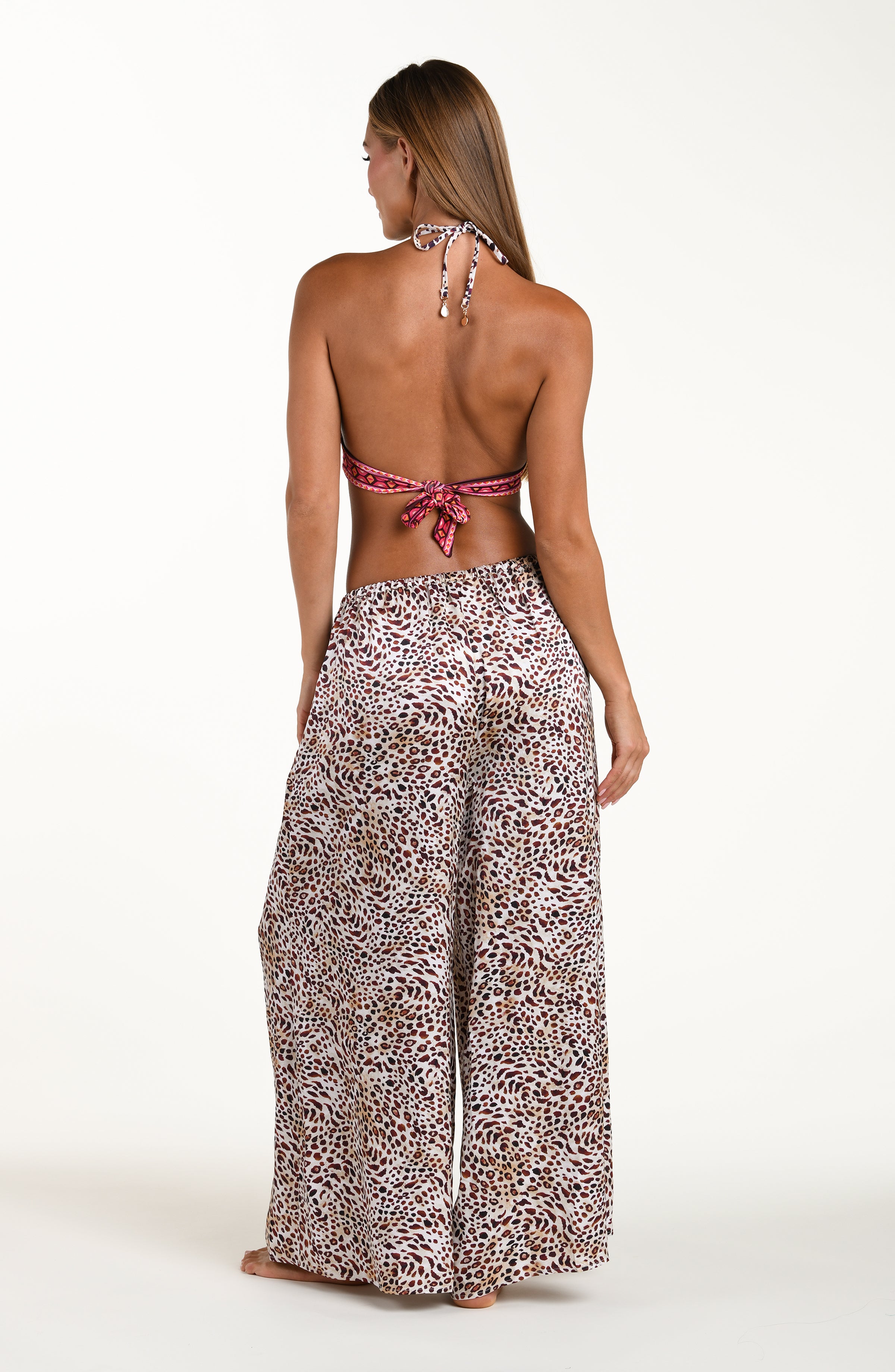 Full body back image of model wearing leopard printed beach pants with an elastic waist and pockets. This is paired with a matching bikini top. 